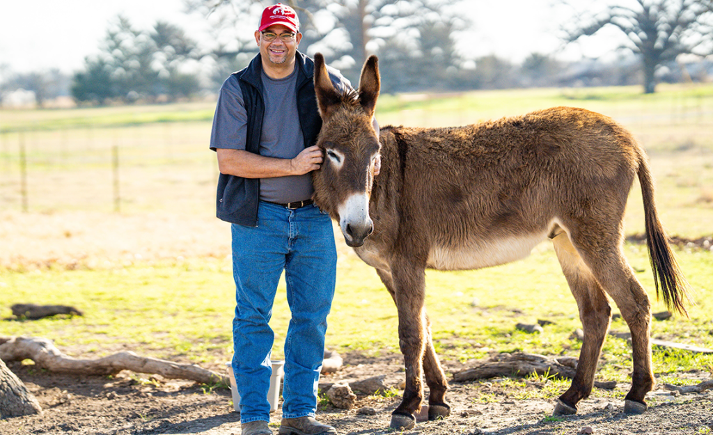 Ed Jamison smiling at camera petting a donkey.