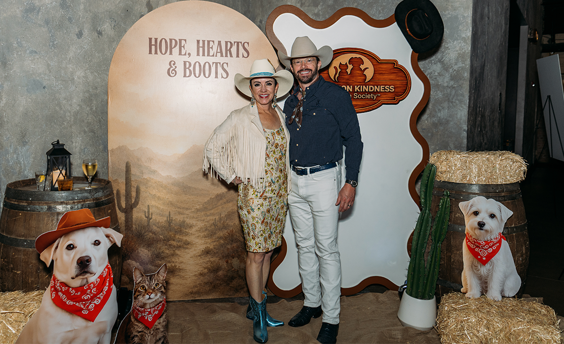 Two people standing in front of a western themed backdrop at Hope, Hearts & Boots