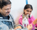 A kitten with two people petting it.